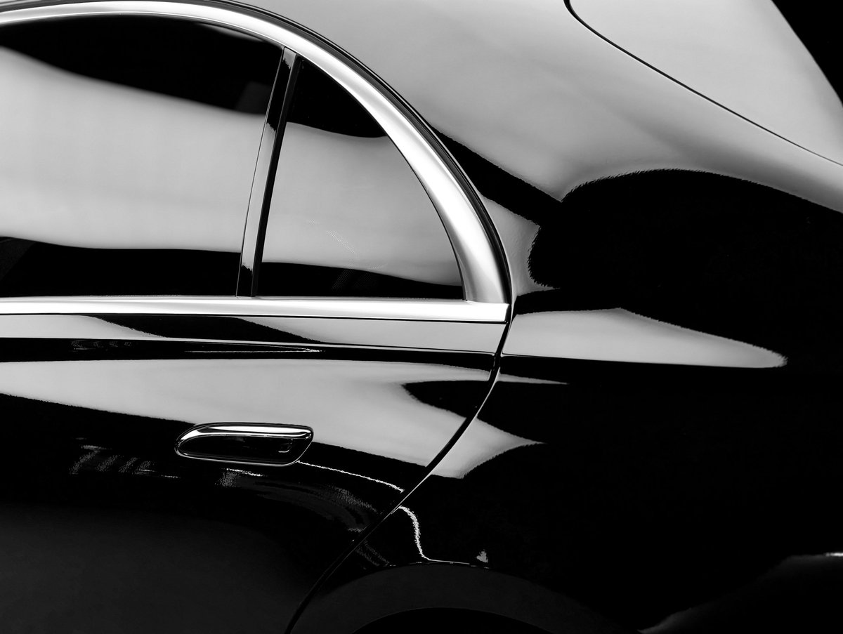 The polished surface of a luxury vehicle reflects light, highlighting its elegant curves and chrome accents in a minimalist composition