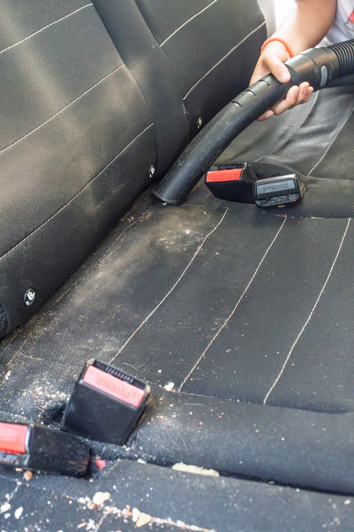 Person removing crumbs and dust from a car interior using a vacuum cleaner